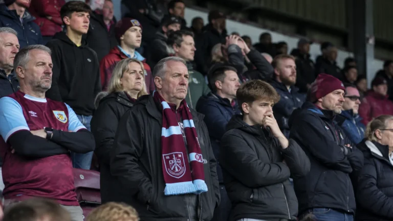 Collectieve groep teleurgestelde Burnley-supporters op de tribune met een Burnley-sjaal.