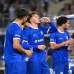 Een groep KAA Gent-spelers in blauwe tenue drinkt water langs het veld.