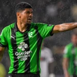 Een Cercle Brugge-speler in groen-zwart tenue gebaart op een nat voetbalveld.