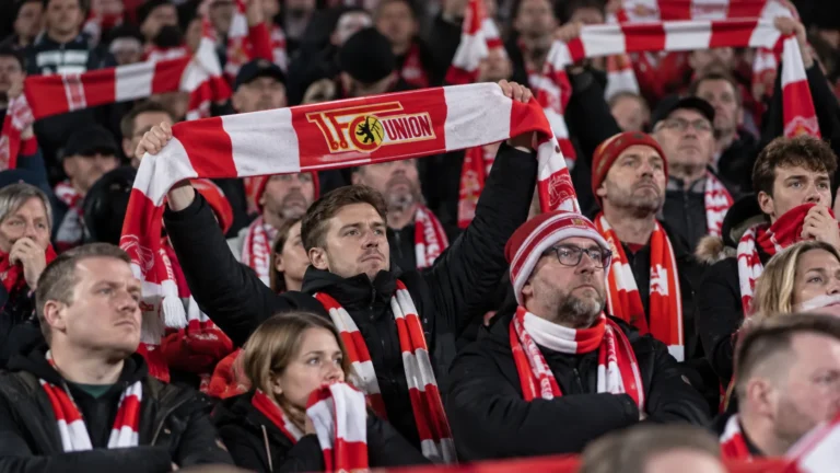 Collectieve groep Union Berlin-supporters met rood-witte sjaals in de tribune.