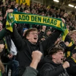 Supporters van ADO Den Haag vieren uitbundig in de tribune met een ADO-sjaal.