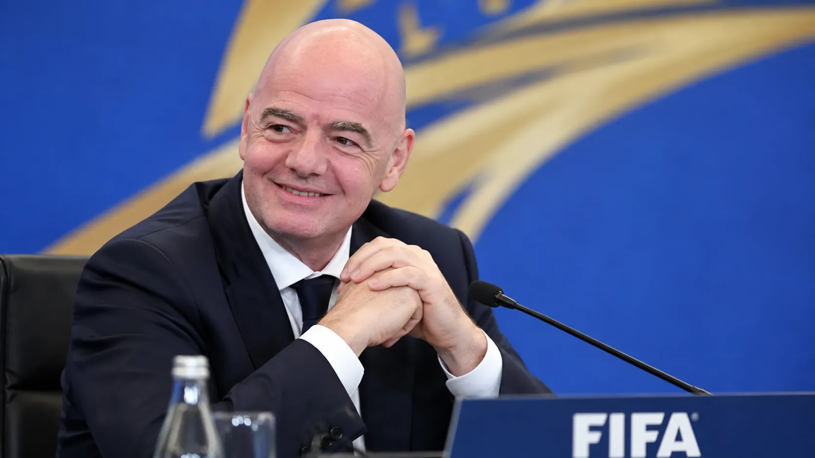 Gianni Infantino in donker pak voor een FIFA-conferentieachtergrond.