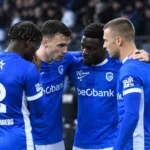 Een groep spelers in blauwe shirts vormt samen een hechte kring op het veld.