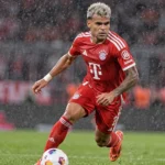 Een Bayern-speler in rood tenue tijdens een regenachtige Bundesliga-wedstrijd.