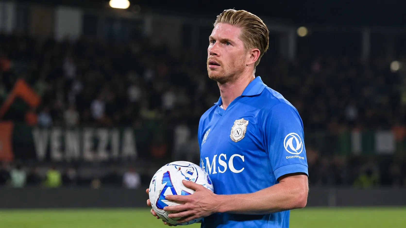 Kevin De Bruyne van Napoli kijkt geconcentreerd op het veld terwijl hij een bal vasthoudt.