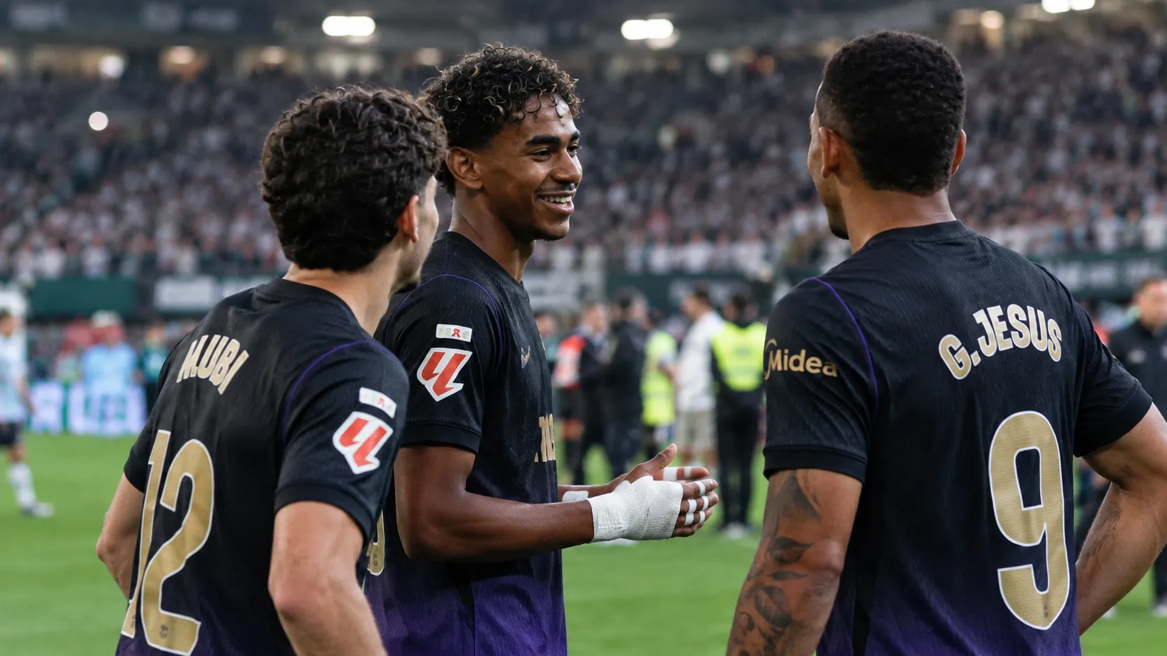 Lamine Yamal staat na de wedstrijd met twee ploegmaats op het veld in donkere wedstrijdshirts.
