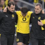 Een geblesseerde Borussia Dortmund-speler wordt langs de zijlijn ondersteund door twee stafleden.