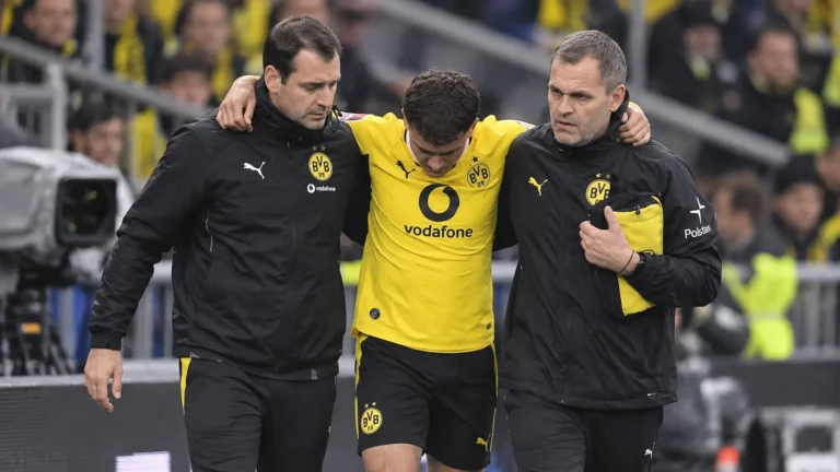 Een geblesseerde Borussia Dortmund-speler wordt langs de zijlijn ondersteund door twee stafleden.