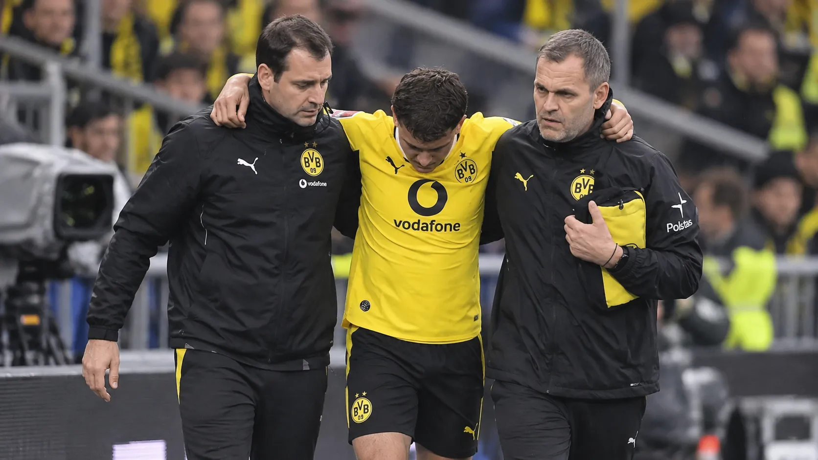 Een geblesseerde Borussia Dortmund-speler wordt langs de zijlijn ondersteund door twee stafleden.