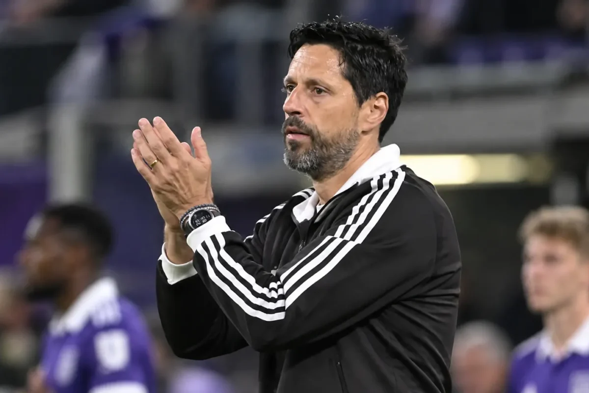 Vitor Bruno applaudisseert langs de zijlijn terwijl Anderlecht-spelers op de achtergrond staan.