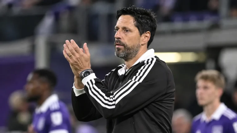 Vitor Bruno applaudisseert langs de zijlijn terwijl Anderlecht-spelers op de achtergrond staan.