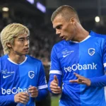 Twee spelers van KRC Genk overleggen naast het veld in blauwe wedstrijdshirts.
