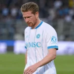 Kevin De Bruyne kijkt neerwaarts op het veld in een wit voetbalshirt.