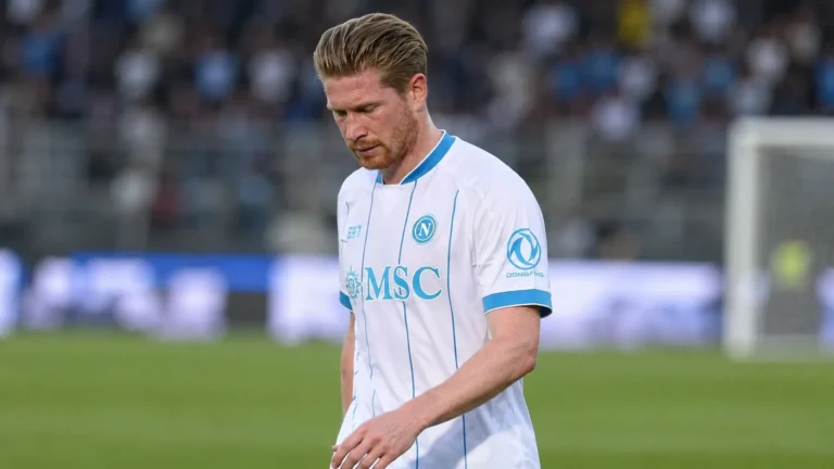 Kevin De Bruyne kijkt neerwaarts op het veld in een wit voetbalshirt.