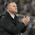 Stijn Vreven in een donkere jas langs de zijlijn van een voetbalstadion.