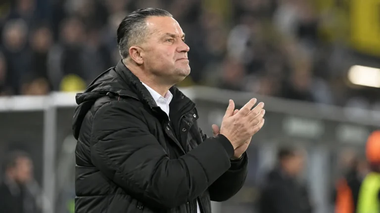 Stijn Vreven in een donkere jas langs de zijlijn van een voetbalstadion.
