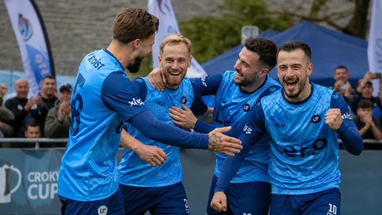 Een groep voetballers in blauwe shirts viert samen langs het veld.