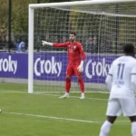Spelers in witte tenues en een doelman in rood bij het doel tijdens een bekerwedstrijd.