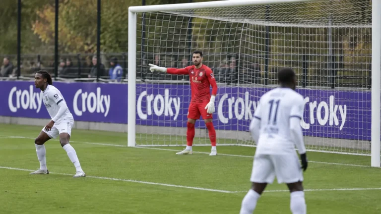 Spelers in witte tenues en een doelman in rood bij het doel tijdens een bekerwedstrijd.