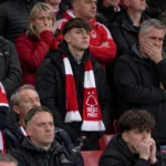 Teleurgestelde supporters van Nottingham Forest op de tribune met een rood-witte clubsjaal.