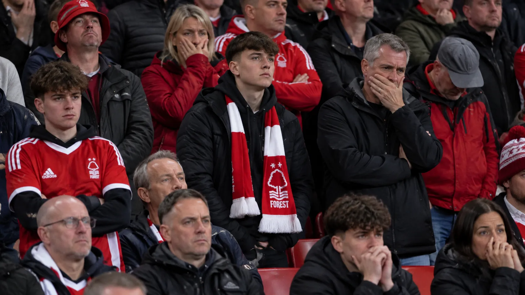Teleurgestelde supporters van Nottingham Forest op de tribune met een rood-witte clubsjaal.