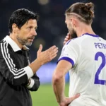 Een Anderlecht-speler in een wit shirt praat na de match op het veld met een staflid.