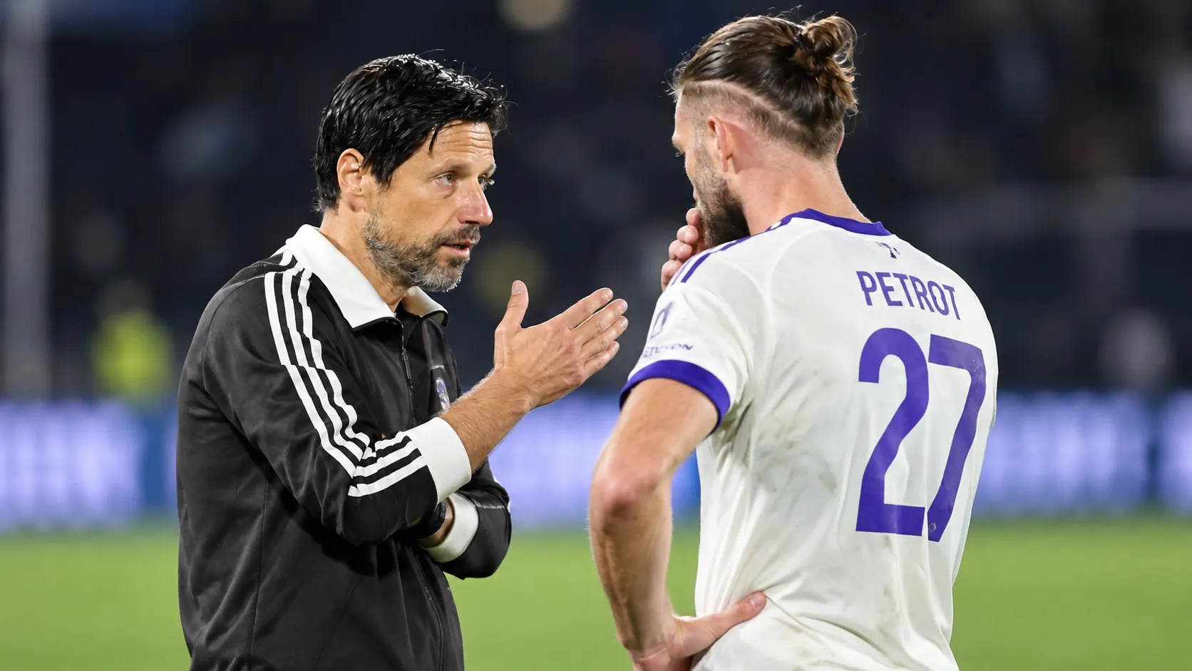 Een Anderlecht-speler in een wit shirt praat na de match op het veld met een staflid.