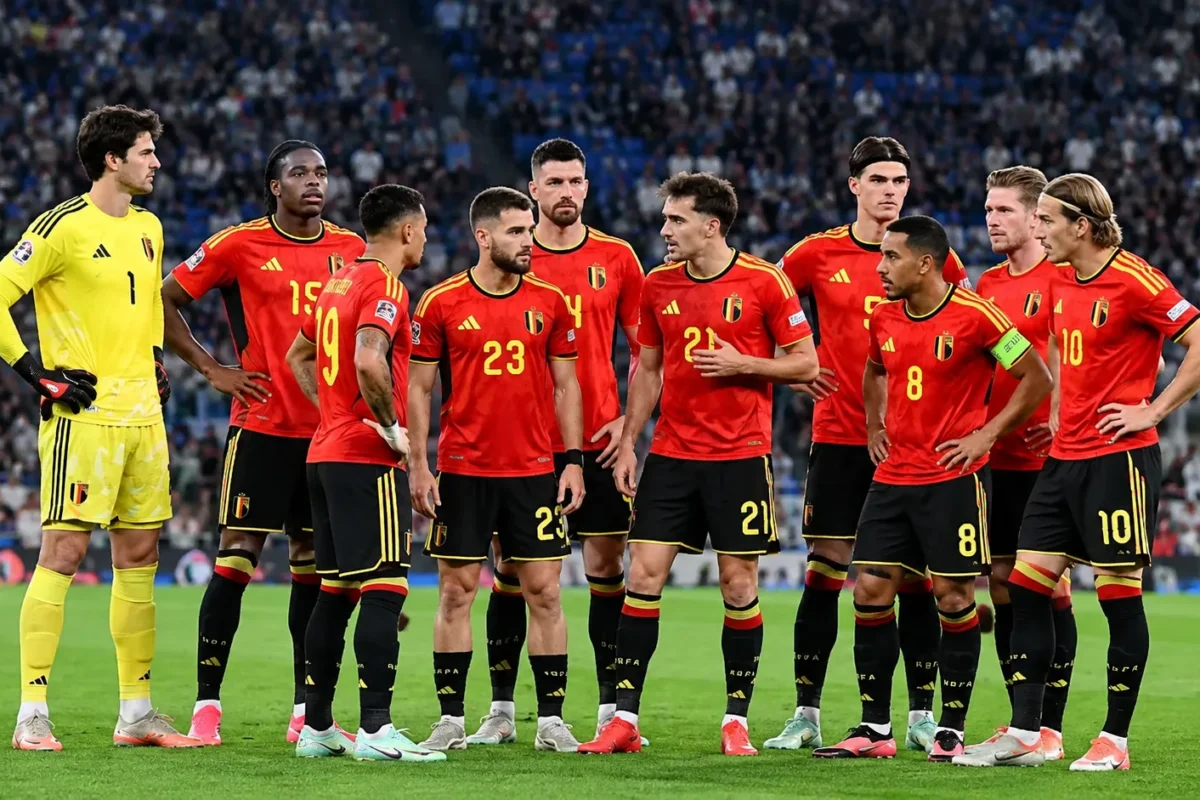 Belgische internationals poseren in rode tenues voor een wedstrijd in een vol stadion.