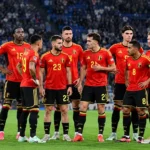 Belgische internationals poseren in rode tenues voor een wedstrijd in een vol stadion.