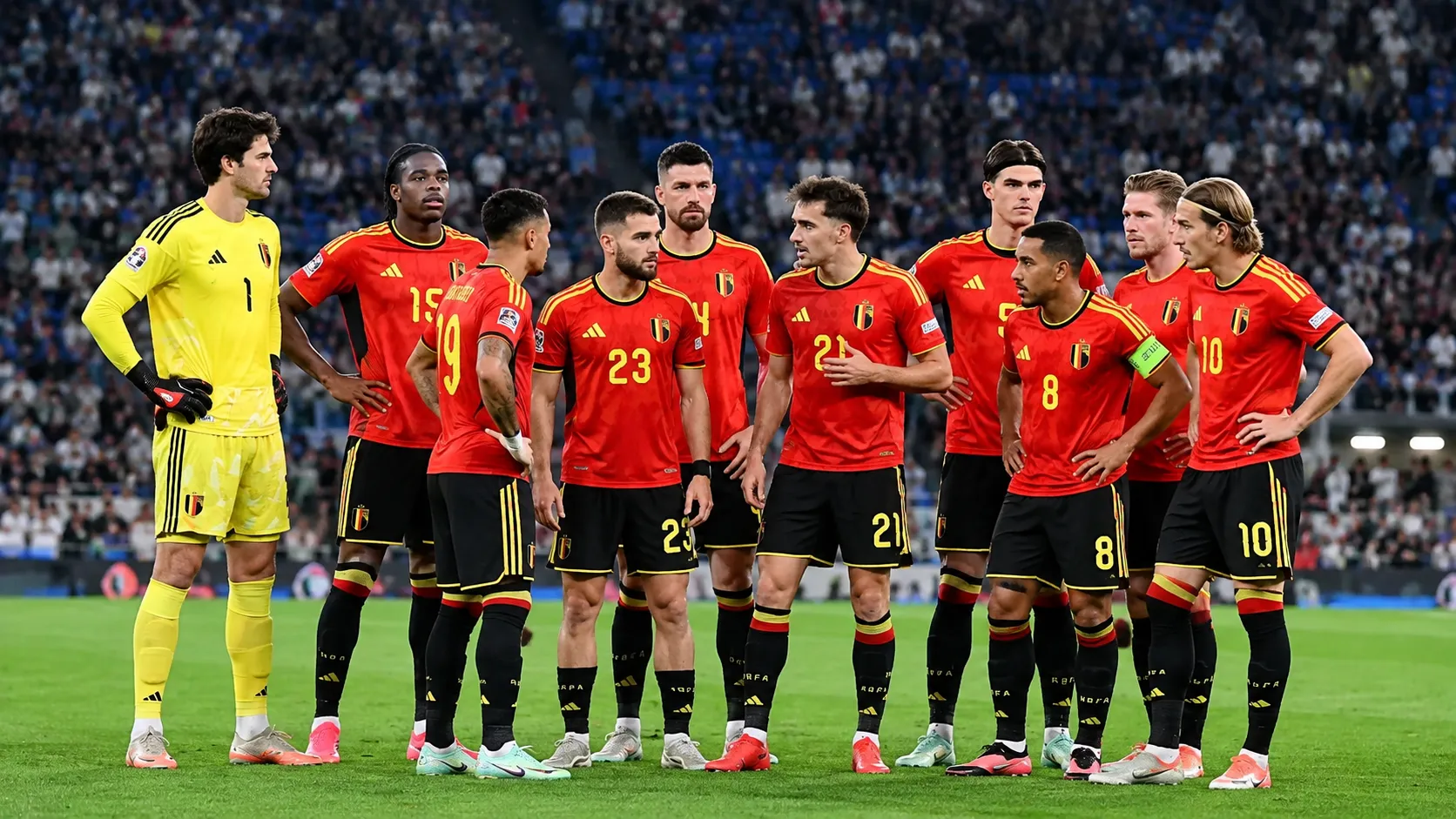 Belgische internationals poseren in rode tenues voor een wedstrijd in een vol stadion.
