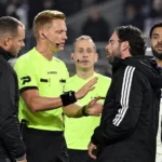 Een scheidsrechter overlegt op het veld met niet-spelende clubmedewerkers tijdens een Belgische bekerwedstrijd.