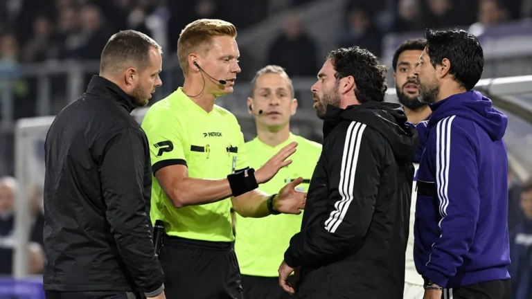 Een scheidsrechter overlegt op het veld met niet-spelende clubmedewerkers tijdens een Belgische bekerwedstrijd.