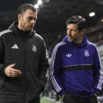 Twee stafleden van Anderlecht wandelen langs de zijlijn van een verlicht stadion.