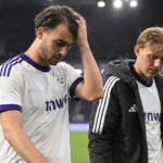 Twee voetballers verlaten na een avondwedstrijd het veld in witte shirts met paarse details.