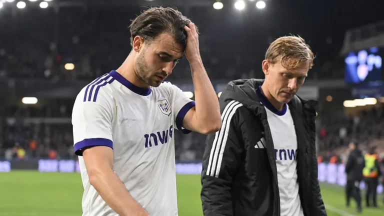 Twee voetballers verlaten na een avondwedstrijd het veld in witte shirts met paarse details.