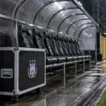 Een lege bezoekersdug-out met een materiaaltrunk van Anderlecht naast het veld.