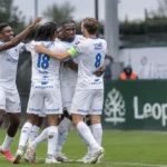 Een groep KRC Genk-spelers in witte wedstrijdtenues viert samen op het veld.
