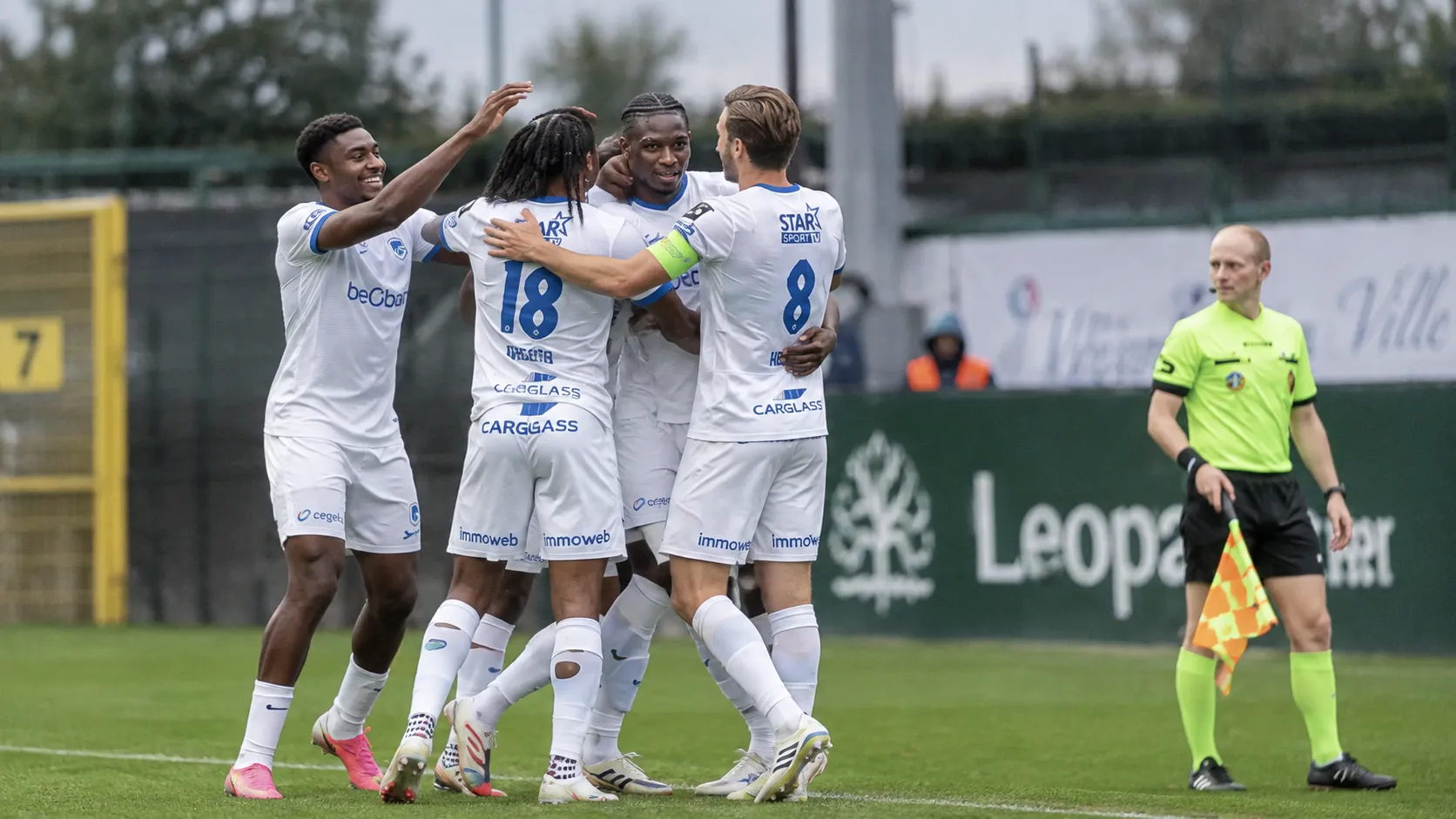 Een groep KRC Genk-spelers in witte wedstrijdtenues viert samen op het veld.