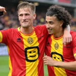 Twee spelers van KV Mechelen vieren samen op het veld in rood-gele shirts.