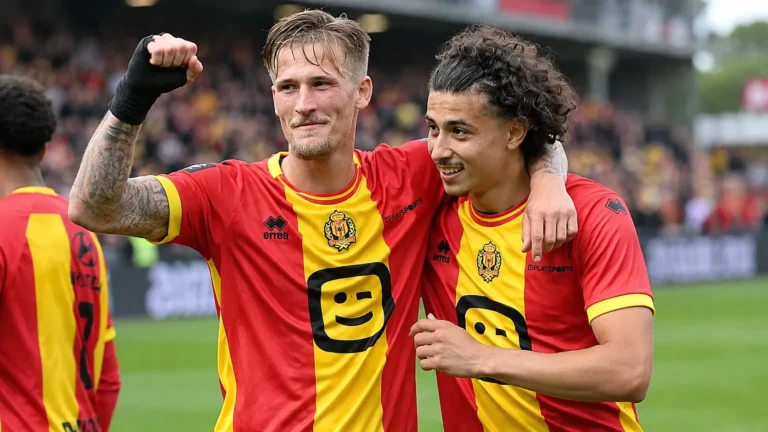 Twee spelers van KV Mechelen vieren samen op het veld in rood-gele shirts.