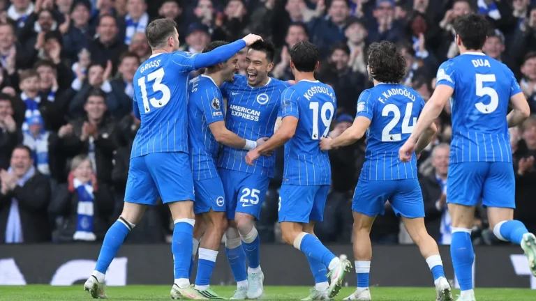 Een groep voetballers in blauw gestreepte shirts viert samen op het veld voor een volle tribune.