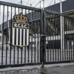 Afgesloten toegangspoort van een voetbalstadion met een Sporting Charleroi-embleem.