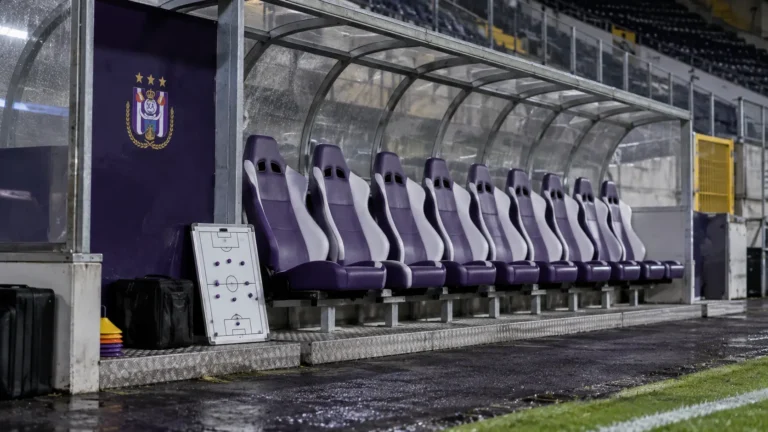 Lege bezoekersdug-out met een klein RSC Anderlecht-embleem op een vast wandpaneel.