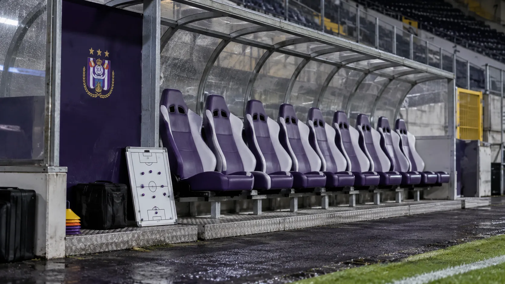Lege bezoekersdug-out met een klein RSC Anderlecht-embleem op een vast wandpaneel.