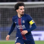 Vitinha in PSG-tenue op een verlicht voetbalveld met een doelnet op de achtergrond.