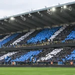 Collectieve Club Brugge-supporters met blauw-zwarte kaarten op de tribune.