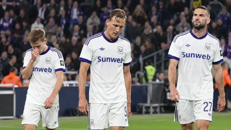 Drie voetballers in witte shirts verlaten zichtbaar ontgoocheld het veld na een wedstrijd.