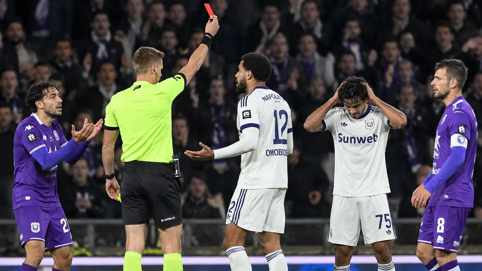 Een scheidsrechter toont een rode kaart tijdens een bekerwedstrijd met spelers op de voorgrond.
