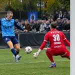 Een speler in blauw en een doelman in rood tijdens een nieuw spelmoment voor doel.