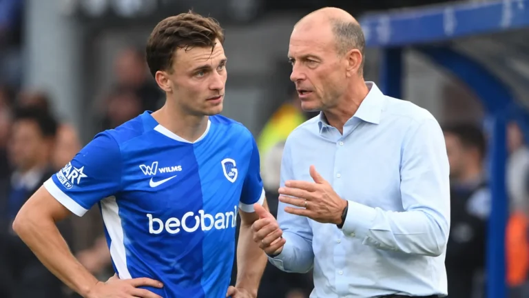 Een voetballer in een blauw shirt overlegt langs de zijlijn met een staflid.